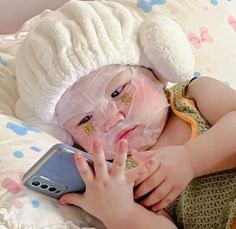 a small child wearing a white hat and holding a cell phone in her hands while laying on a bed