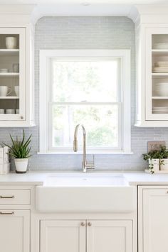 a kitchen with white cabinets and an open window above the sink is filled with dishes