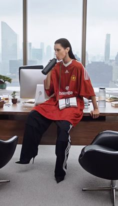 a woman sitting in an office chair with her foot on the desk while talking on a cell phone