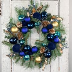 a wreath with blue, gold and green ornaments hanging on a white wooden door frame