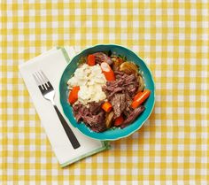 a blue bowl filled with meat and vegetables on top of a yellow checkered table cloth