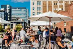 a group of people sitting around tables with umbrellas on top of them in the city