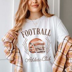 Gear up for game day with our Football Athletic Club Comfort Color Tee. Crafted for comfort and style, this tee is perfect for fans who want to show their support in a laid-back yet spirited way. Emblazoned with the emblem of our Football Athletic Club, this tee exudes team spirit and camaraderie. Whether you're cheering from the stands or watching from home, our tee ensures you'll be representing your team in style. Made from premium materials, this tee offers unparalleled comfort and durabilit Collegiate Graphic Print T-shirt For Game Day, Fall Varsity T-shirt With Logo Print, Collegiate White Top For Football Season, Varsity T-shirt With Team Logo For Football Season, White Collegiate Top For Football Season, Game Day Sports Fan T-shirt With Crew Neck, Team-colored Tops For Sports Events In Fall, Varsity Tops For Sports Events In Fall, Varsity Tops For Fall Sports Events