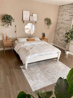 a white bed sitting on top of a wooden floor next to a mirror and potted plants