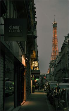 the eiffel tower is lit up at night in front of cars parked on the street