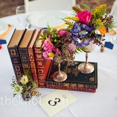 the table is set with books and flowers in vases on top of each book