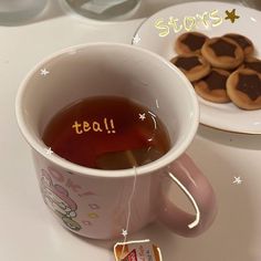 a cup of tea next to some cookies on a plate with the word tea written in it