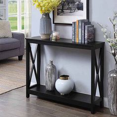 a black table with vases and flowers on it in front of a gray couch