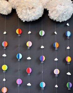 paper lanterns and clouds hanging from strings on a gray wall with white tissue pom poms