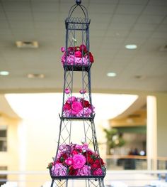 three tiered metal tower with pink flowers on it's sides in an indoor setting