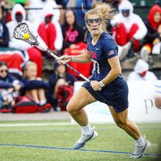 a female lacrosse player in action on the field during a game with spectators behind her