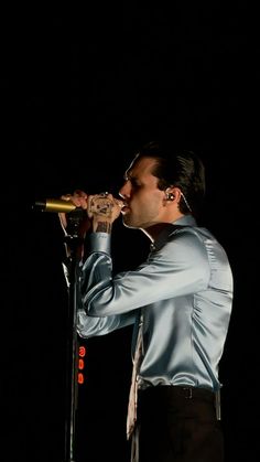 a man in a blue shirt and tie holding a microphone to his mouth while standing on stage