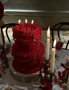 a red cake sitting on top of a table covered in candles