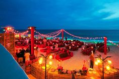 an outdoor seating area on the beach is lit up with candles and lights at night