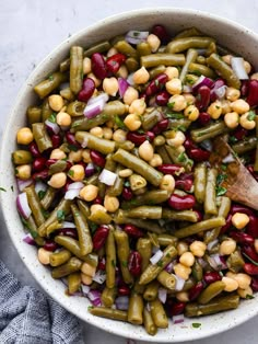 a bowl filled with beans, onions and green beans next to a wooden spatula