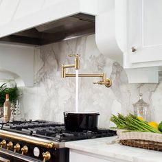 a kitchen with marble counter tops and gold faucets on the stove top, surrounded by white cabinets