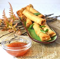 some food is sitting on a plate next to a bowl of dipping sauce and leaves