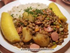 a white plate topped with potatoes and lentils next to rice on top of a wooden table