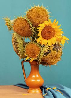 a vase filled with lots of sunflowers on top of a wooden table next to a blue wall