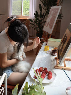 a woman sitting at a table holding a small white dog in her lap while she holds raspberries