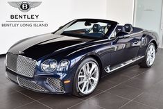 a blue bentley car is parked in front of a bentley logo on a white wall