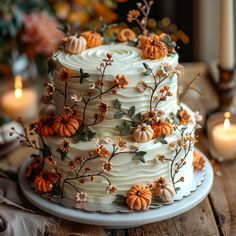 a three layer cake decorated with pumpkins and flowers on a table next to candles