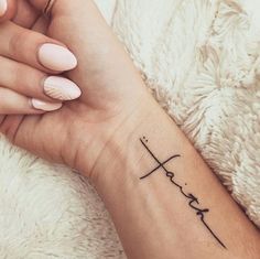 a woman's wrist tattoo with the word faith written in cursive font