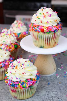 cupcakes with white frosting and sprinkles on a cake stand