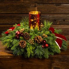 a christmas arrangement with pine cones, berries and candlesticks on a wooden table