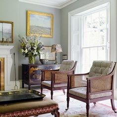 a living room with two chairs and a table in front of a fire place that has a painting on the wall