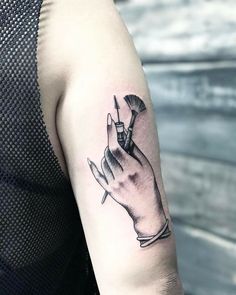 a black and white photo of a hand holding a brush tattoo on the left arm