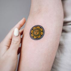 a woman's arm with a small yellow and black sunflower tattoo on it