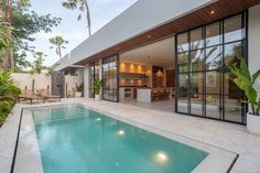 an outdoor swimming pool surrounded by palm trees and patio furniture with sliding glass doors leading to the kitchen