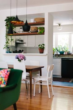 a dining room table and chairs with plants on the shelves above them in a kitchen