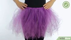 a woman wearing a purple tutu skirt with her hands on her hips, standing in front of a white background