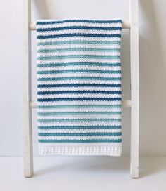 a blue and white striped knitted blanket on a wooden chair against a white wall