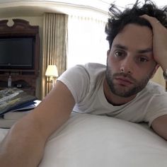 a man laying on top of a bed next to a lamp and a tv set