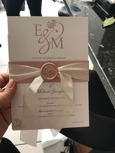 a person holding up a wedding card with a ribbon around the front and back of it