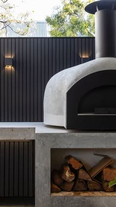 an outdoor pizza oven sitting on top of a cement block next to some firewood