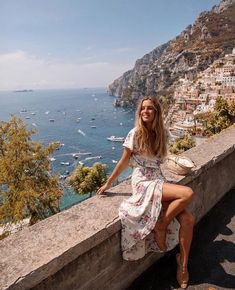 a woman is sitting on a ledge overlooking the ocean