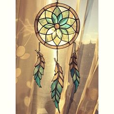 a stained glass dream catcher hanging from a window sill in front of a curtain