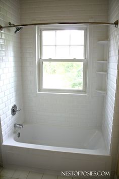 a bath tub sitting under a window next to a tiled floor and white tile walls