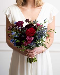 a woman wearing a white dress holding a bouquet of purple and red flowers in her hands