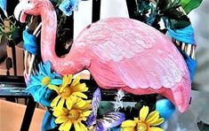 a pink flamingo statue sitting on top of a table next to flowers and butterflies