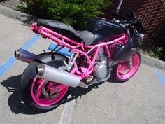 a pink and black motorcycle parked in a parking lot next to some bushes on the sidewalk