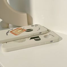 two nintendo wii remotes sitting next to each other on a white counter top in front of a phone holder