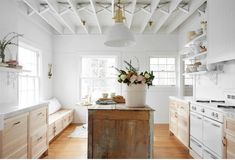 a kitchen with white walls and wooden floors has flowers in a vase on the island