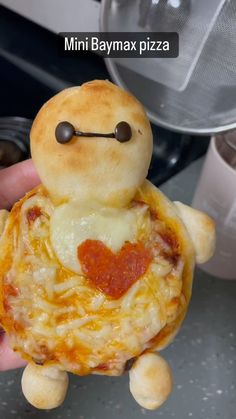 someone is holding up a mini pizza with a face on it's head and arms