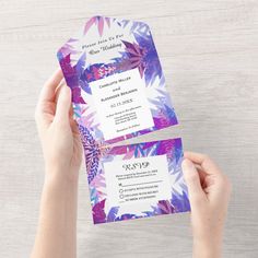 two people holding up wedding cards with flowers on them, one is purple and the other is white