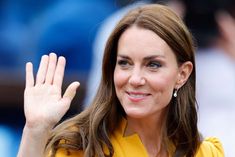 a woman waves to the crowd while wearing a yellow dress